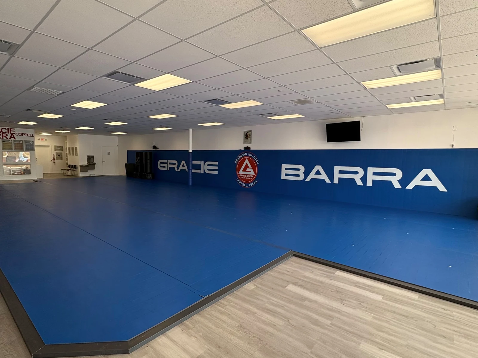 Blue mats in front of the Gracie Barra wall with the red shield logo inside the Coppell academy